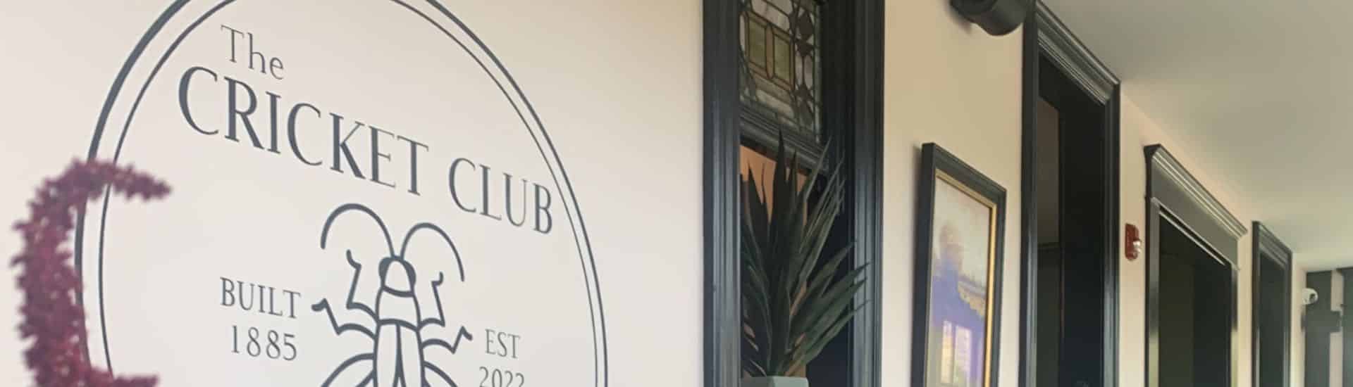 Wall of property painted white with green trim and wainscotting and large The Cricket Club logo