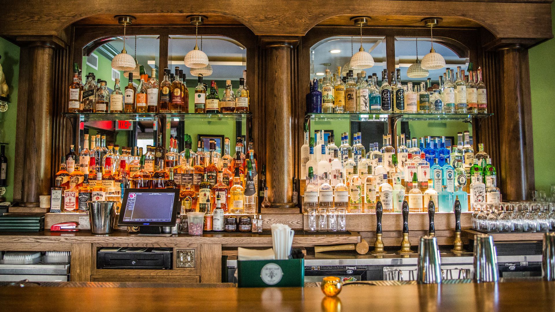 Large wooden bar with leather bar stools and large wooden display case full of bottles of alcohol